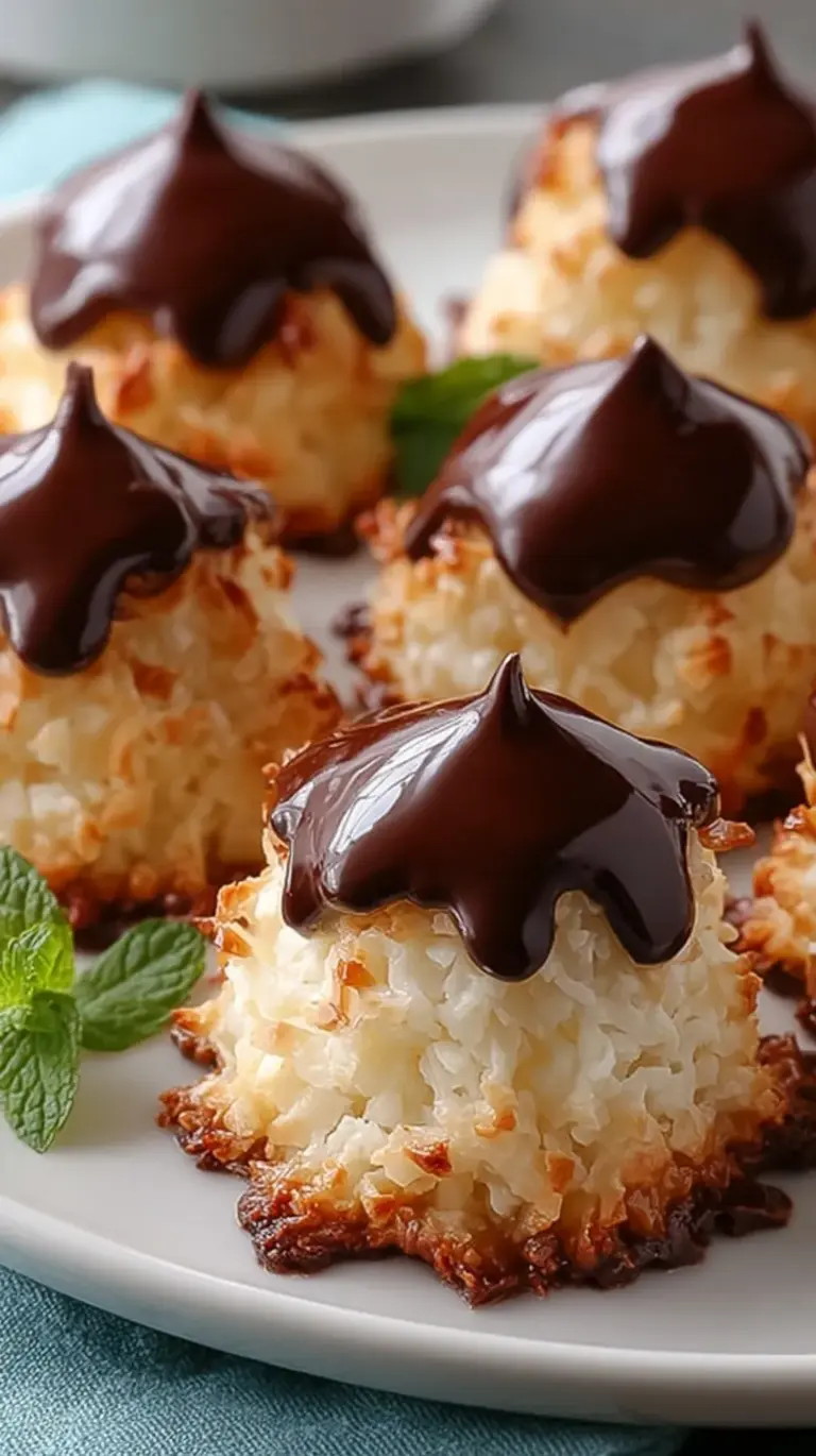 Golden coconut macaroon cookies topped with dark chocolate kisses and flaky sea salt on a baking sheet.