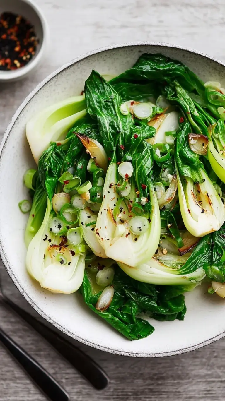 A vibrant green bowl of freshly cooked garlic ginger bok choy, garnished with sesame seeds.
