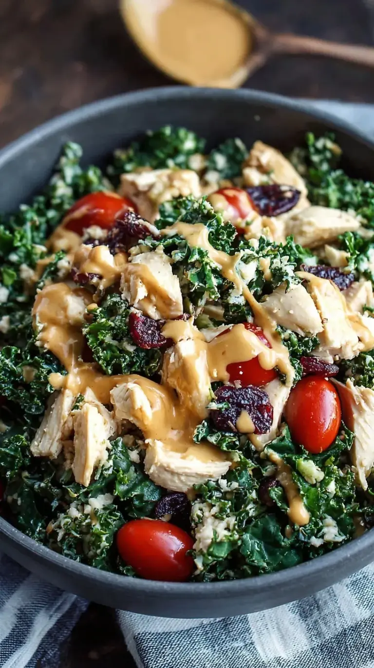 A vibrant healthy kale chicken salad with sliced grilled chicken, avocado, and red peppers in a white bowl.