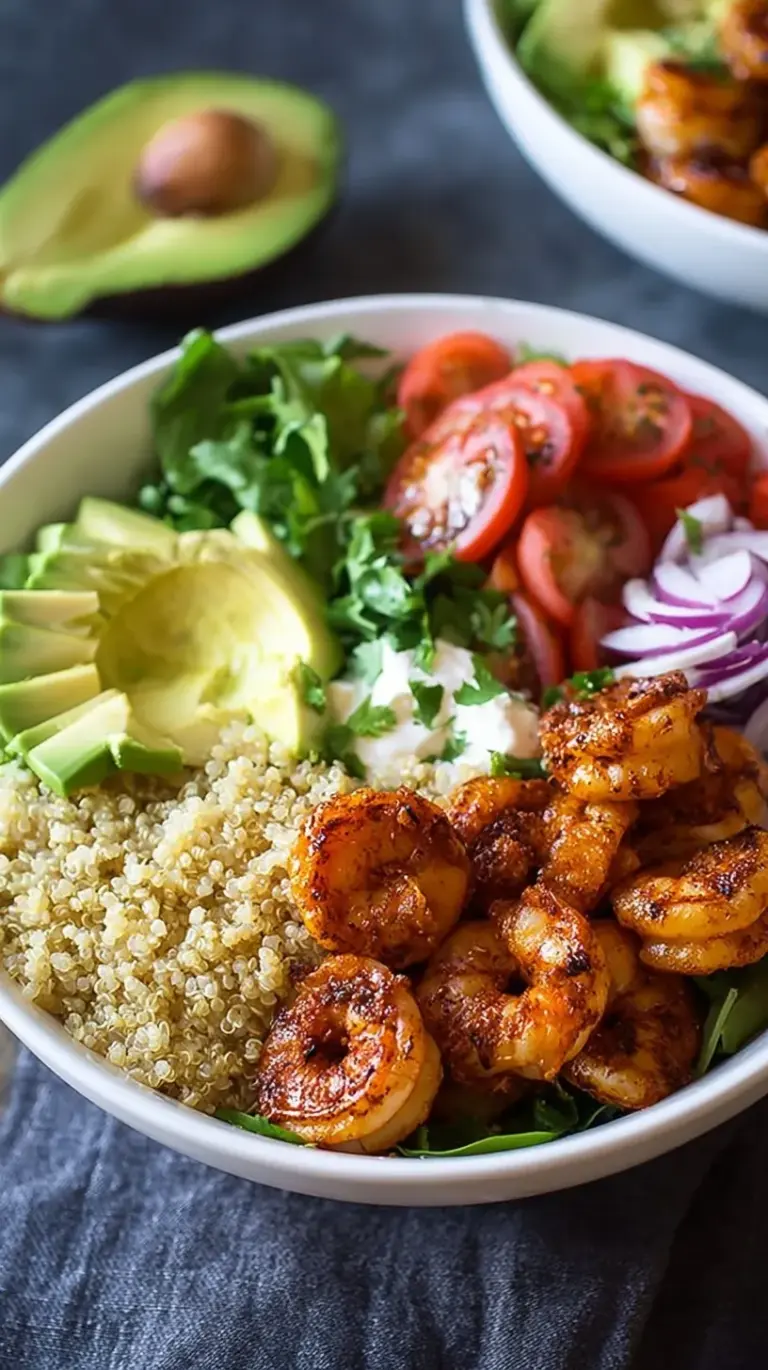 A vibrant quinoa bowl topped with seared shrimp, sliced avocado, cherry tomatoes, and fresh lime.